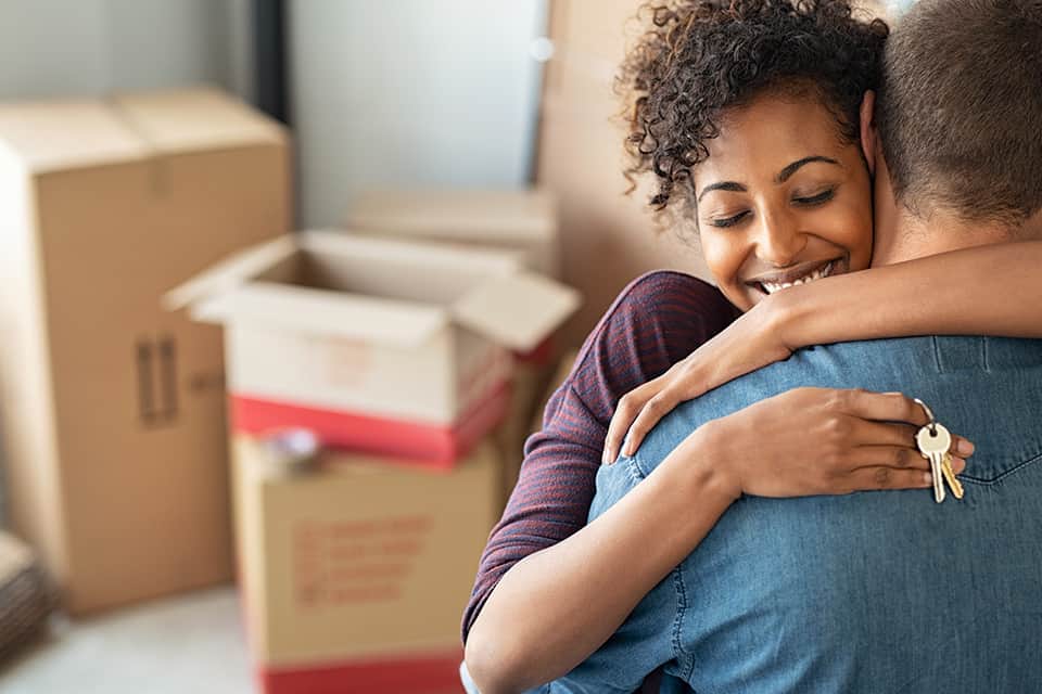 Woman hugs man in new house as they are unpacking boxes
